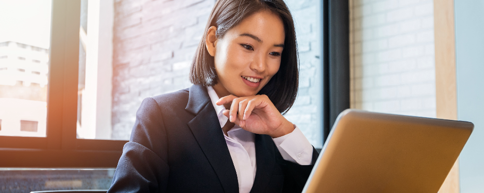 image of female Asian white collar employee worker sitting in front of a laptop smiling