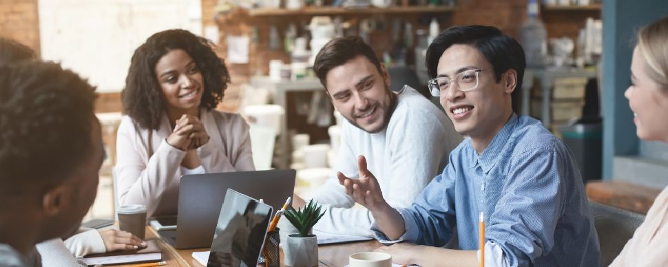 A diverse group of white-collar professionals sitting around a table, smiling, and having a discussion.