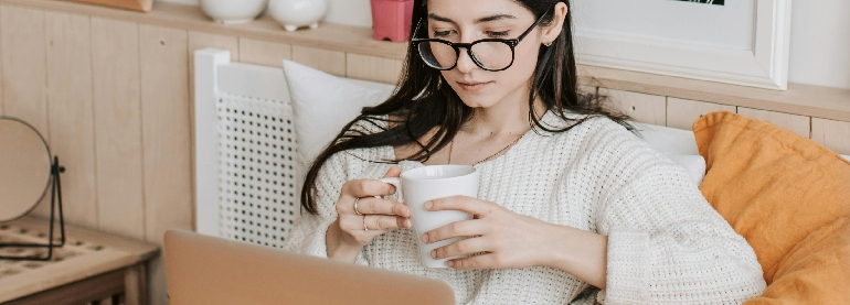 A woman holding a mug while looking at her computer screen