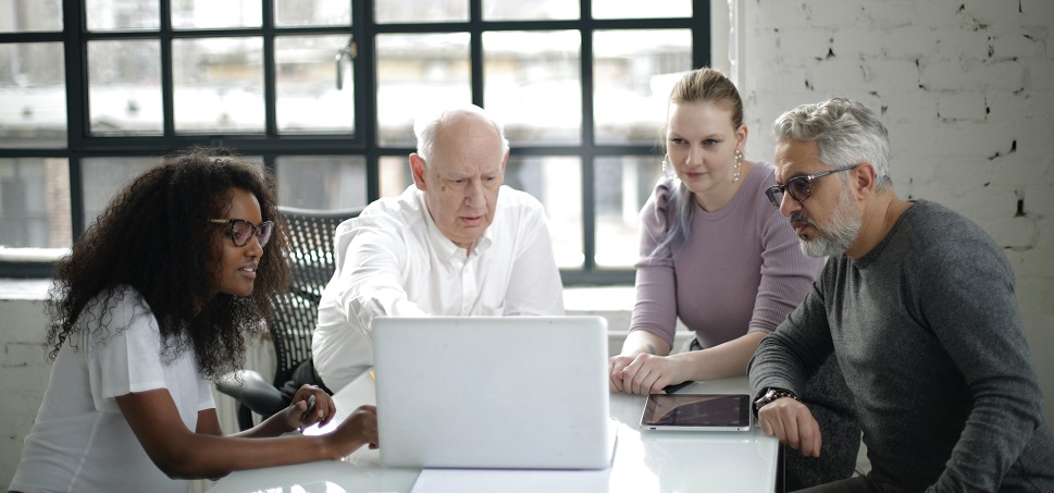 A group of four professionals of different age groups seated and looking at a laptop screen, illustrating an age-inclusive work environment