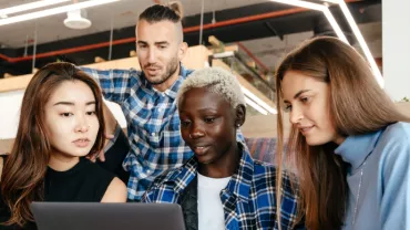 Four working professionals of different race and gender looking at computer screen