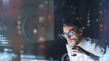 Man analyzing data on a computer screen with graphs in a dimly lit room.