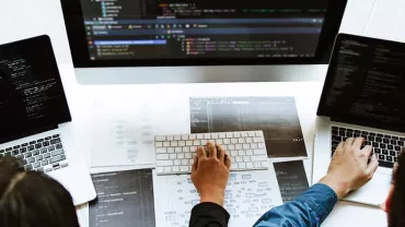 Three people working on laptops with code on the screens.