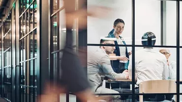 Business meeting in a modern glass-walled office with people discussing.