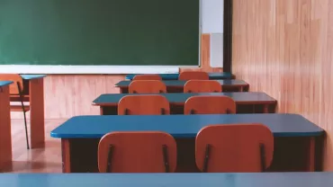 Empty classroom with wooden desks and a green chalkboard.