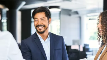 Man in a suit smiling while shaking hands in an office setting.