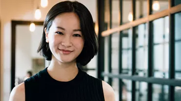 Person smiling in a modern office hallway with glass walls.