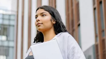 Person holding a laptop standing outside a modern building