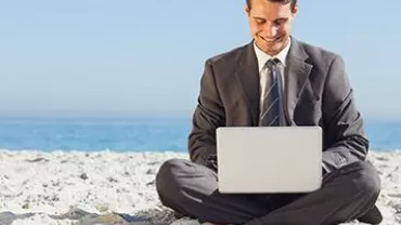 Businessman sitting on the beach using a laptop.