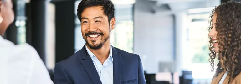 Man in a suit smiling while shaking hands in an office setting.