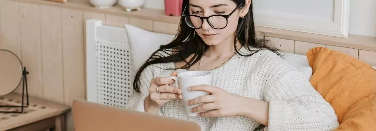 A woman holding a mug while looking at her computer screen